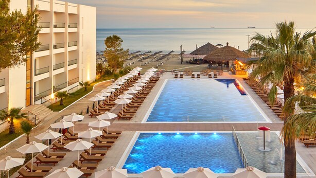 Zona de piscina en un resort con tumbonas y sombrillas, una piscina grande y vistas al mar.