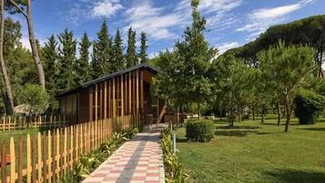 A wooden cabin with a checkered pathway leading to it, surrounded by trees and a wooden fence.