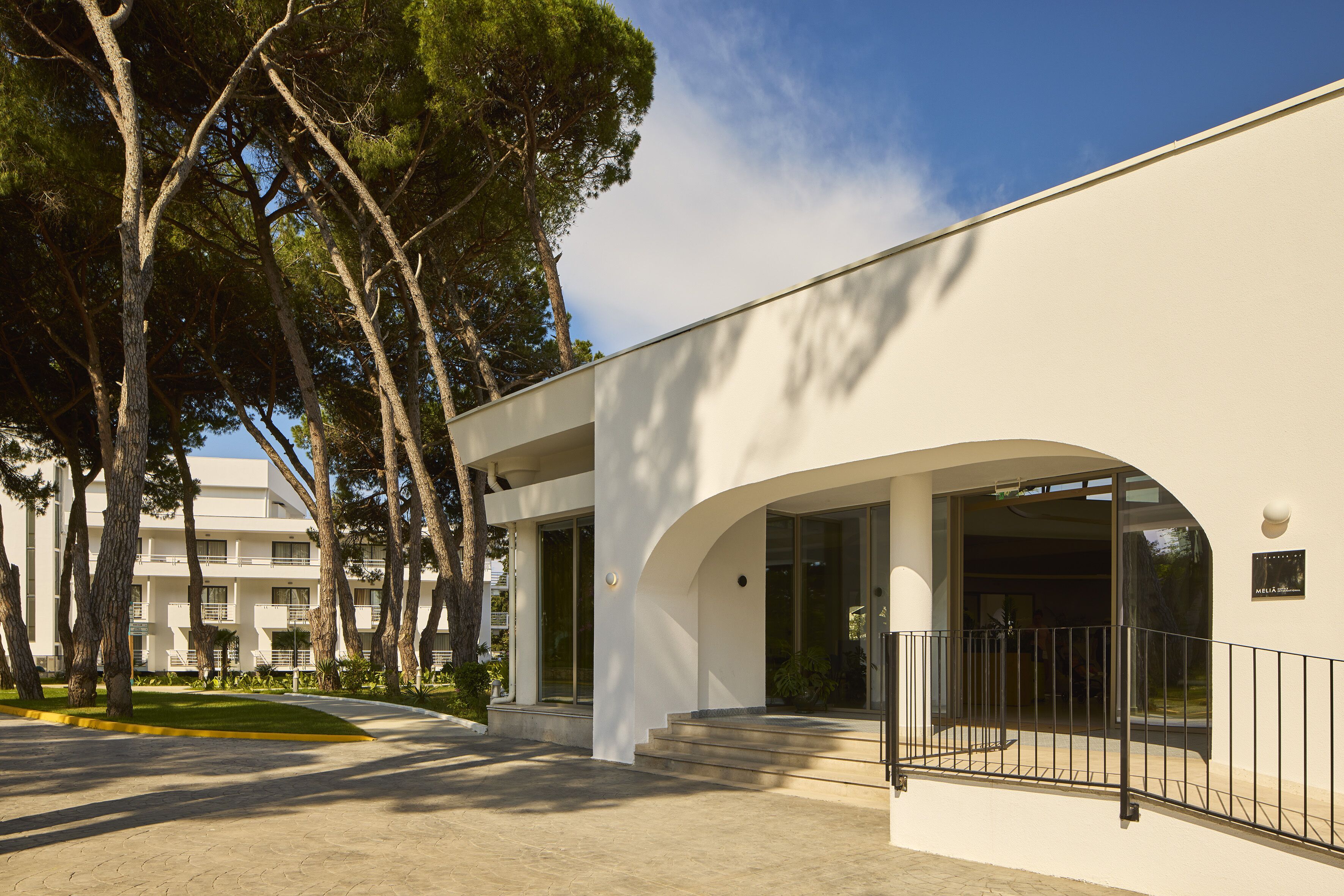 Un edificio moderno con fachada blanca, ventanas grandes y un acceso cubierto con escalones.