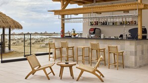 Un bar junto a la playa con sillas de mimbre y una barra con botellas y vasos.