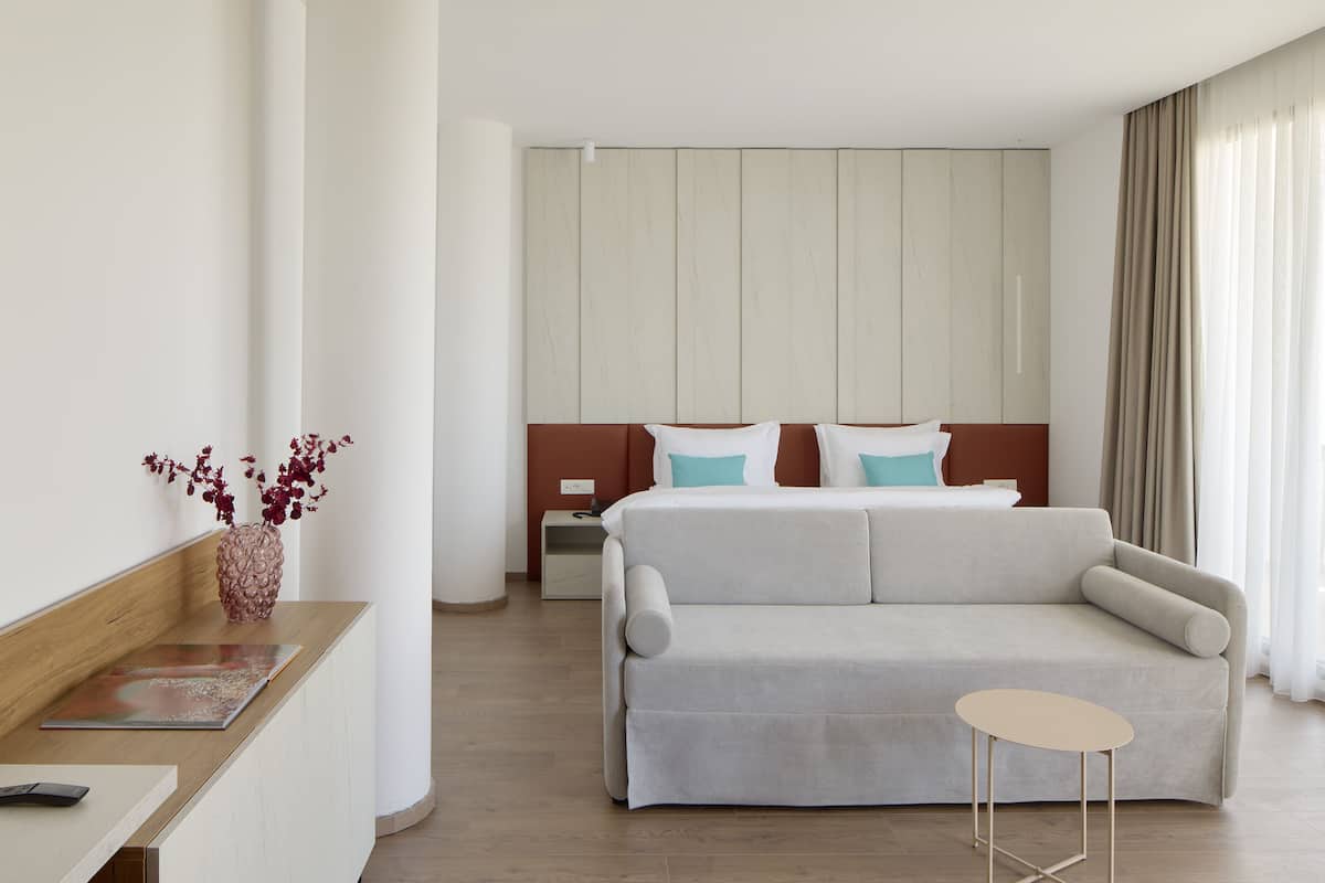 A modern hotel room with a bed, a sofa, a small table, and a vase with flowers.
