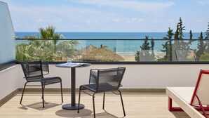 Un balcón con dos sillas y una mesa, con vista a una playa y al océano.