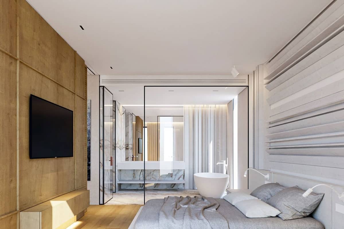A modern bedroom with a large bed, a TV mounted on the wall, and a bathroom visible through a glass partition.