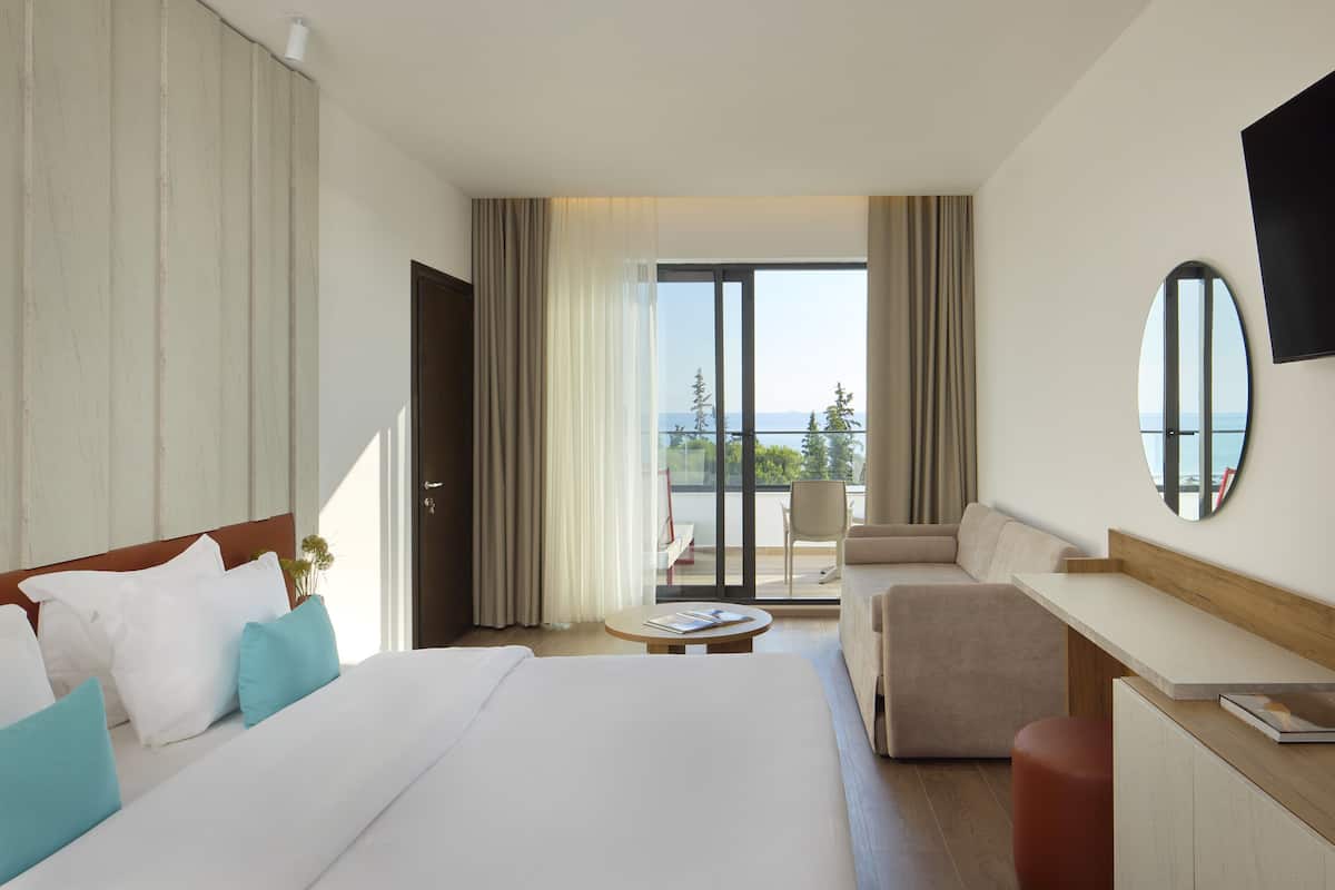 A hotel room with a bed, a sofa, a desk, and a view of the outdoors.