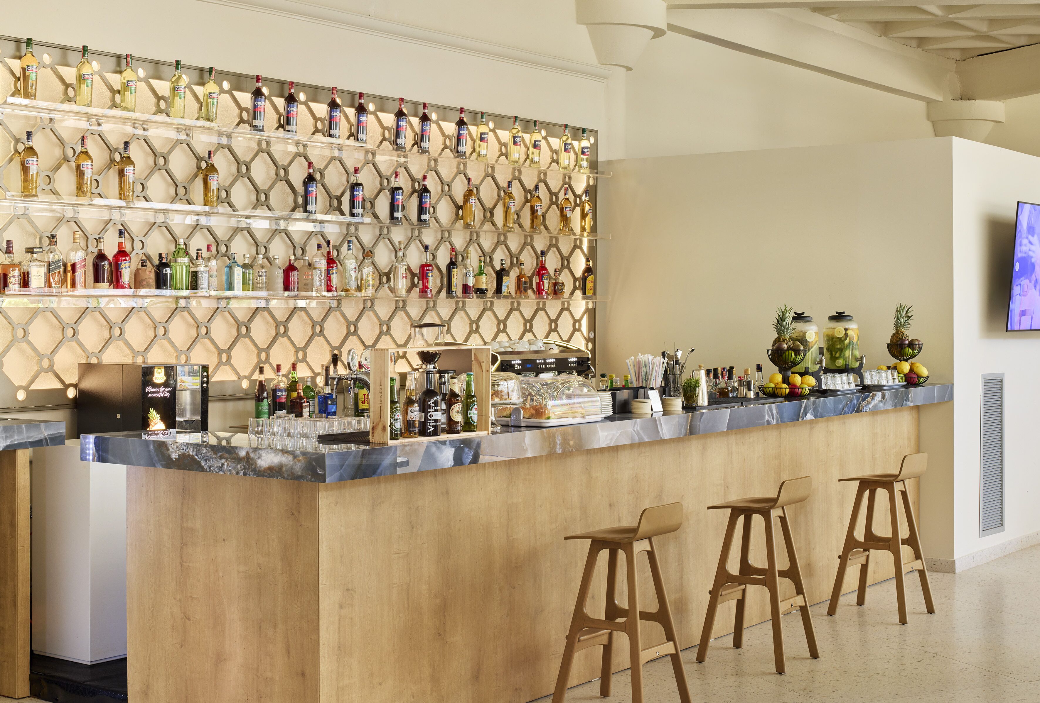 A bar area with a wooden counter, multiple shelves of liquor bottles, and three wooden stools.