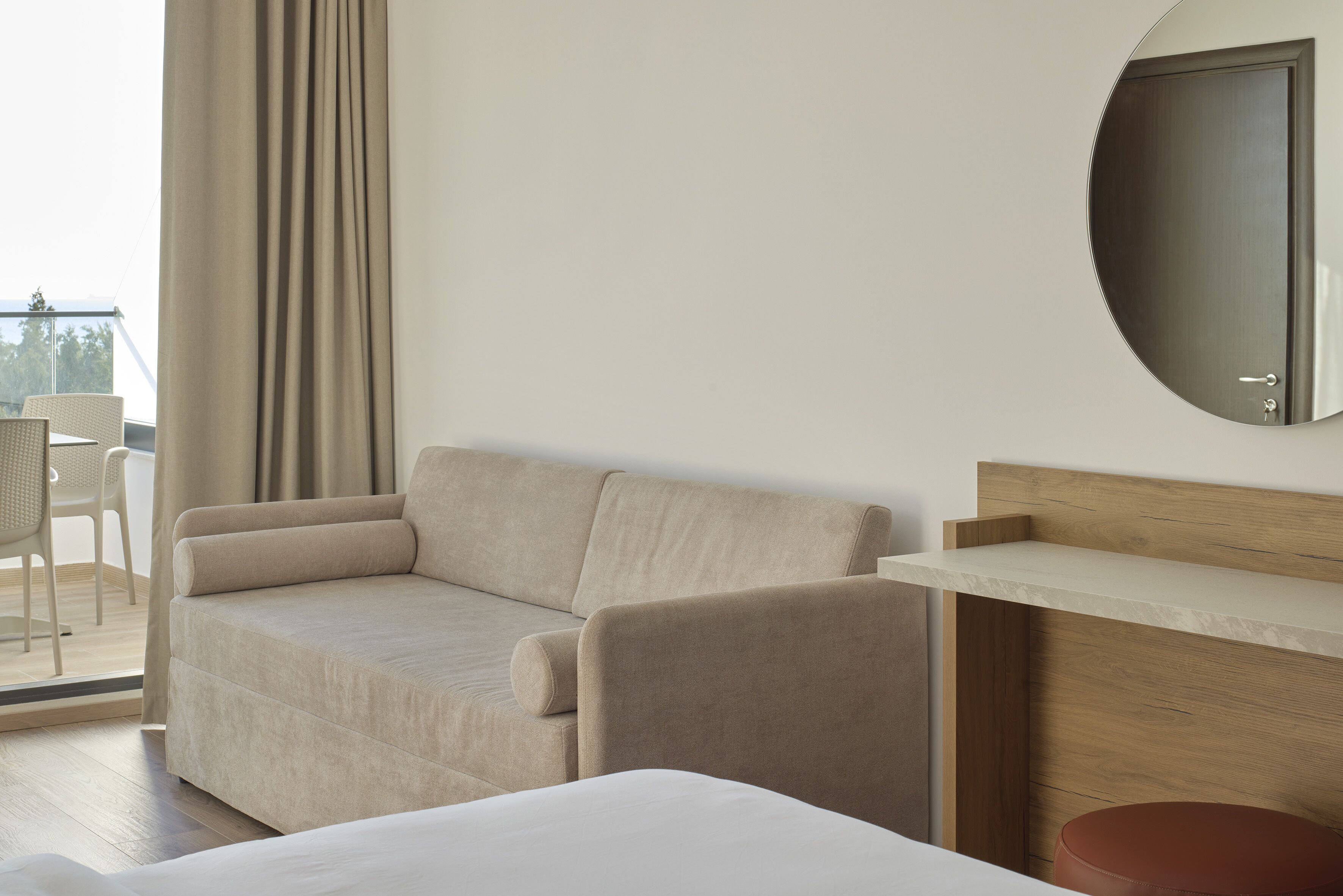 Habitación de hotel con sofá, cama, cabecero de madera, una mesita y vistas al exterior.
