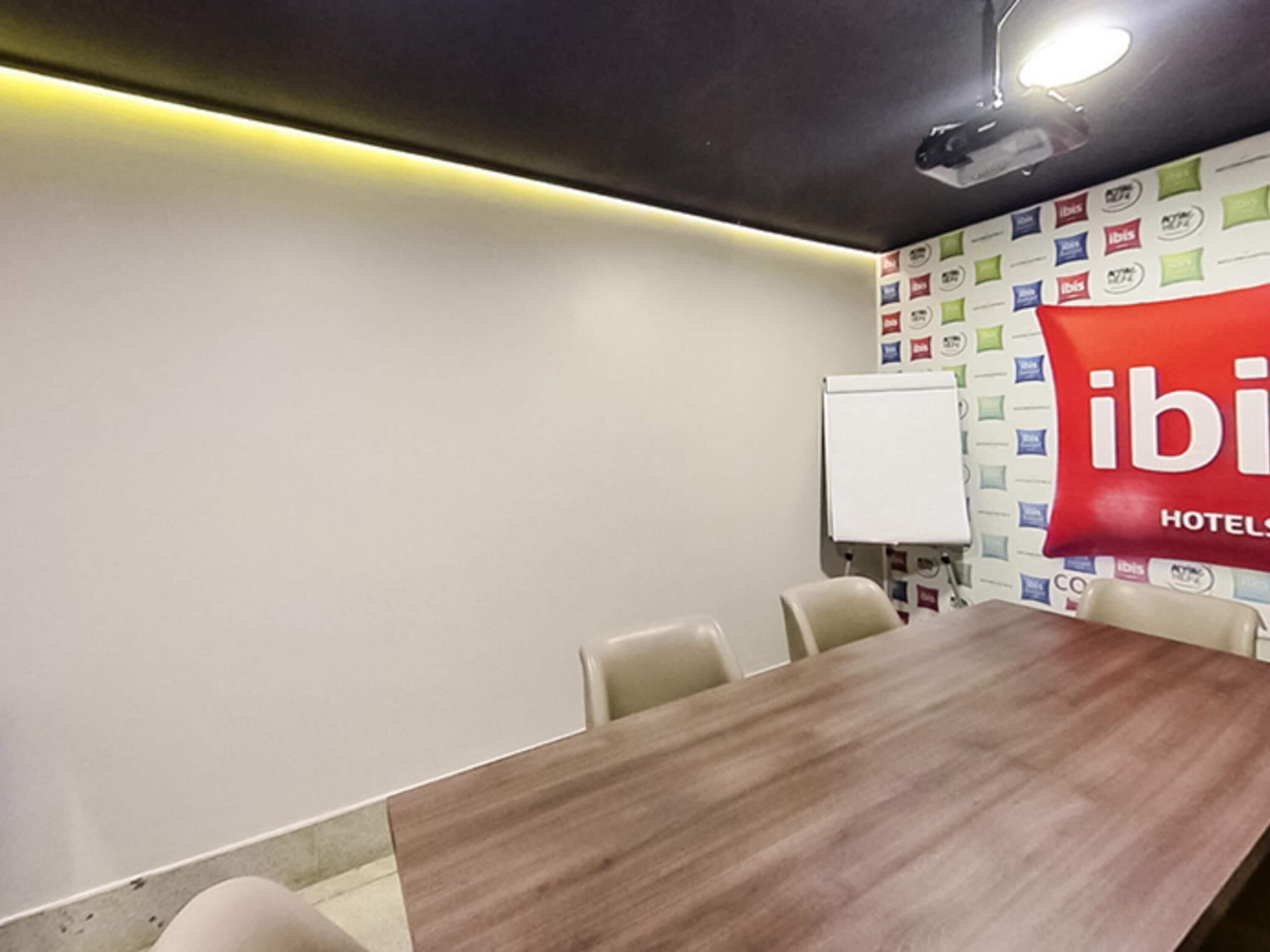 Uma sala de conferências com mesa de madeira, quadro branco e parede com vários logotipos.