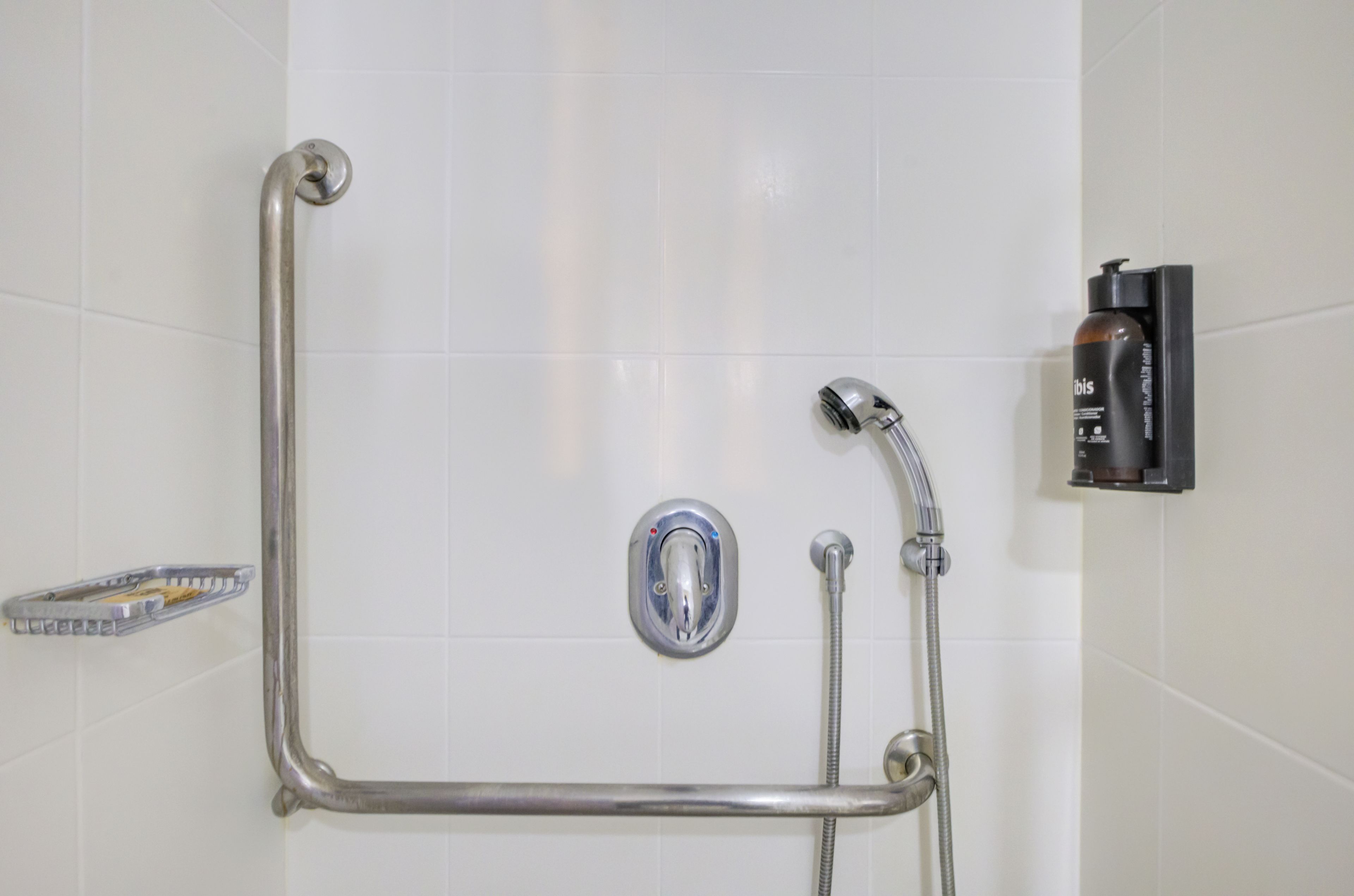 A shower area with a handheld showerhead, a handheld shower attachment, and a bottle of shampoo.