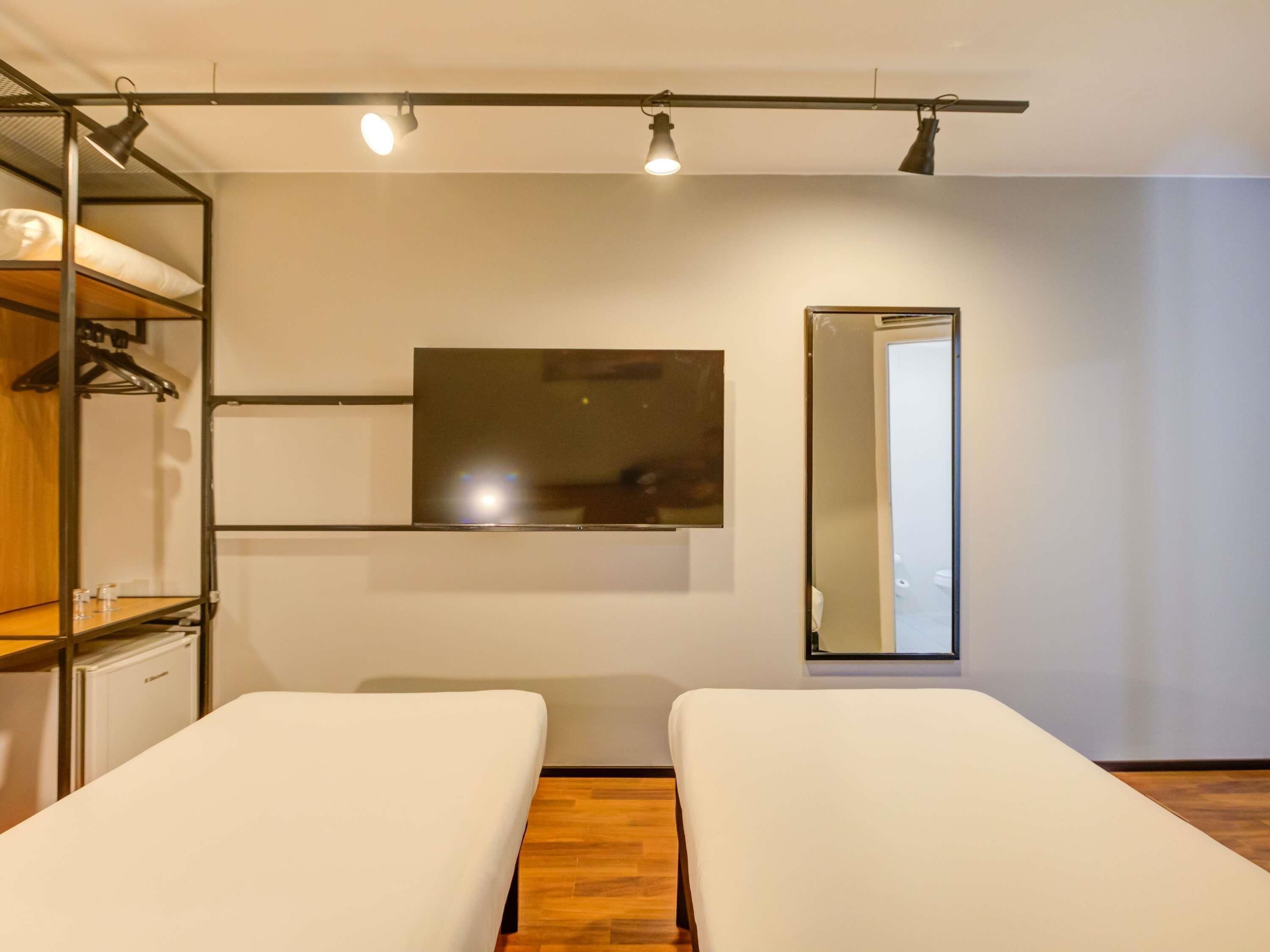 Habitació moderna amb lliteres, televisió de pantalla plana, mirall i terra de fusta.