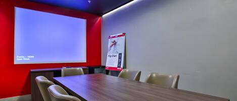 Une salle de conférence avec une grande table, des chaises de couleur beige, un écran de projection et un tableau mobile fixé au mur.