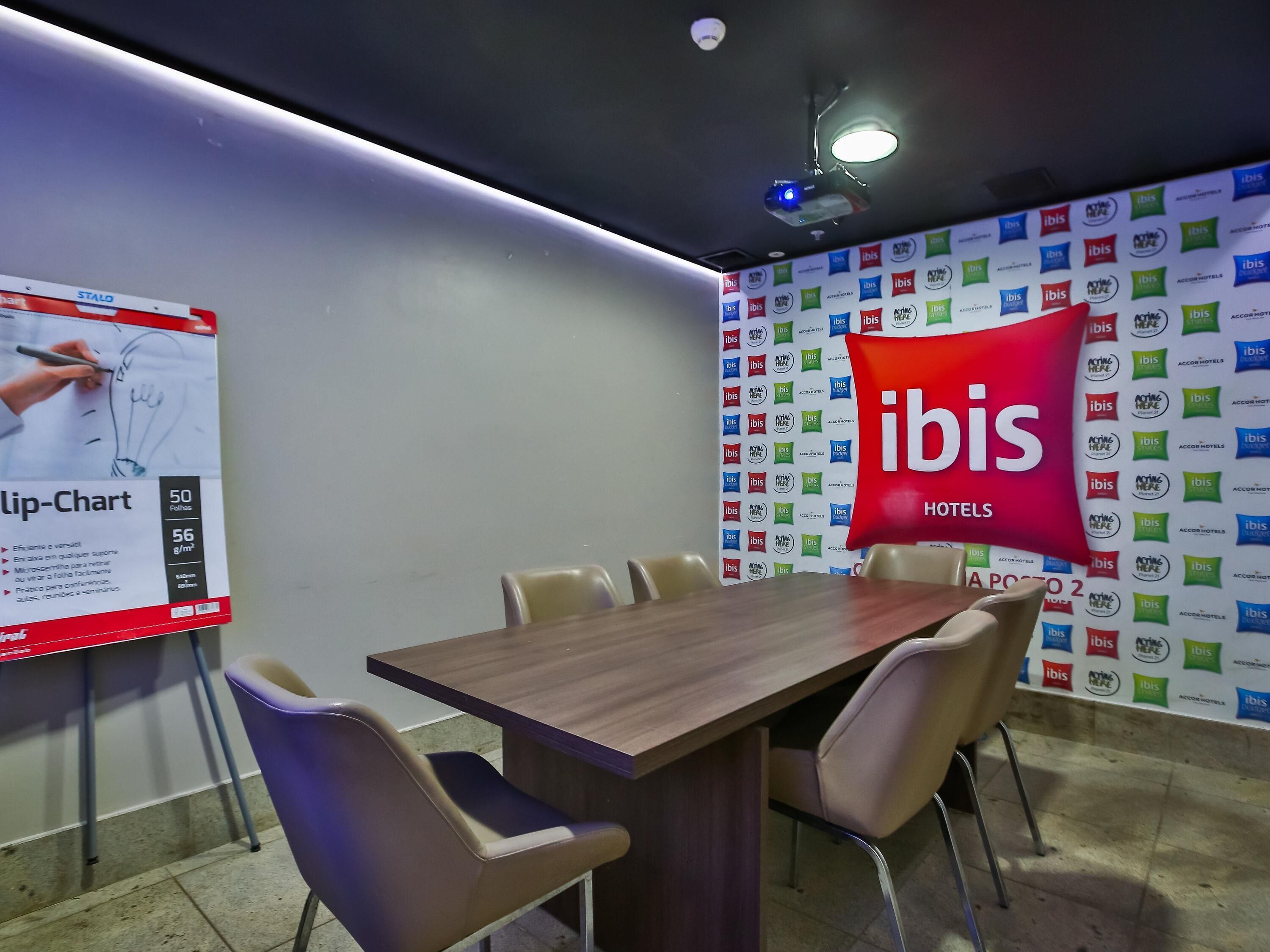 A conference room with a wooden table, beige chairs, a flip chart, and a wall with multiple hotel logos.