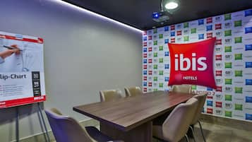 A conference room with a wooden table, beige chairs, a flip chart, and a wall with multiple hotel logos.
