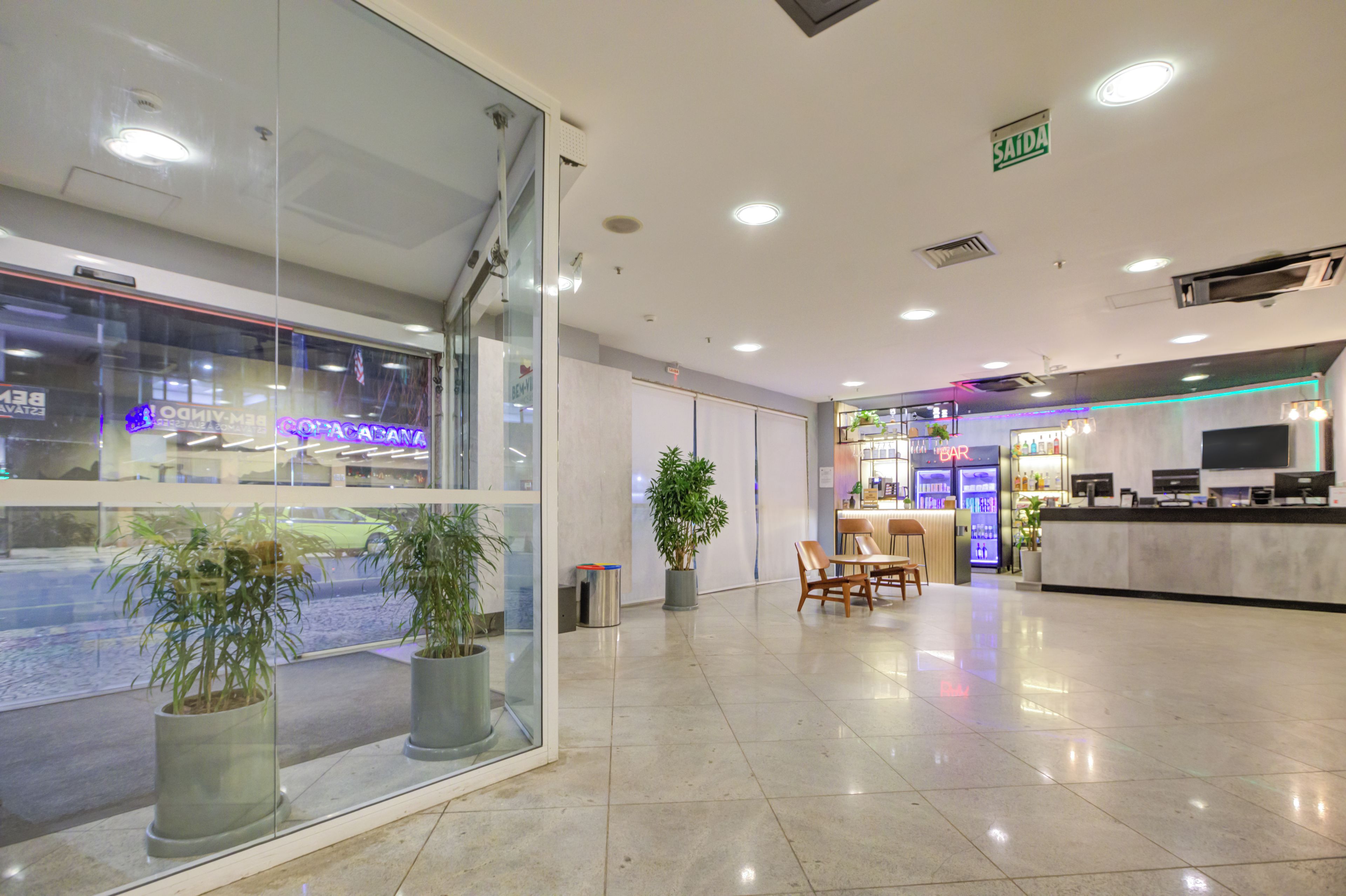 Een moderne hotel lobby met een receptiebalie, zithoek en een glazen wand met uitzicht op de straat.