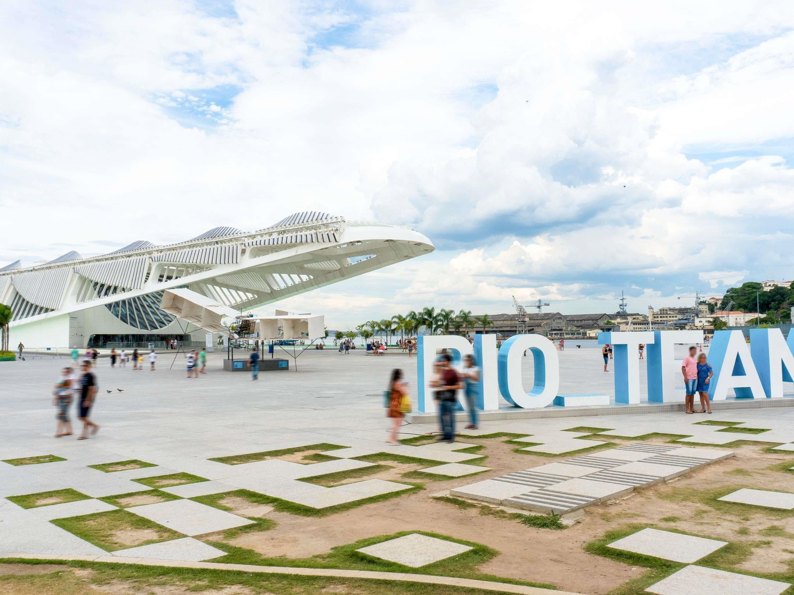 A modern architectural structure with a unique design, a spacious plaza with geometric patterns, and the text 'RIO TEAM' prominently displayed.