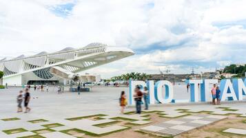 Een moderne architecturale constructie met een uniek ontwerp, een ruimtelijk plein met geometrische patronen, en de tekst 'RIO TEAM' opvallend in het zicht.