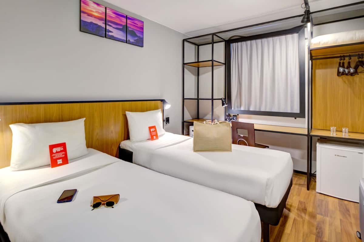 Ein Hotelzimmer mit zwei Betten, einem Schreibtisch, einem Kleiderschrank und einer kleinen Küchenzeile.