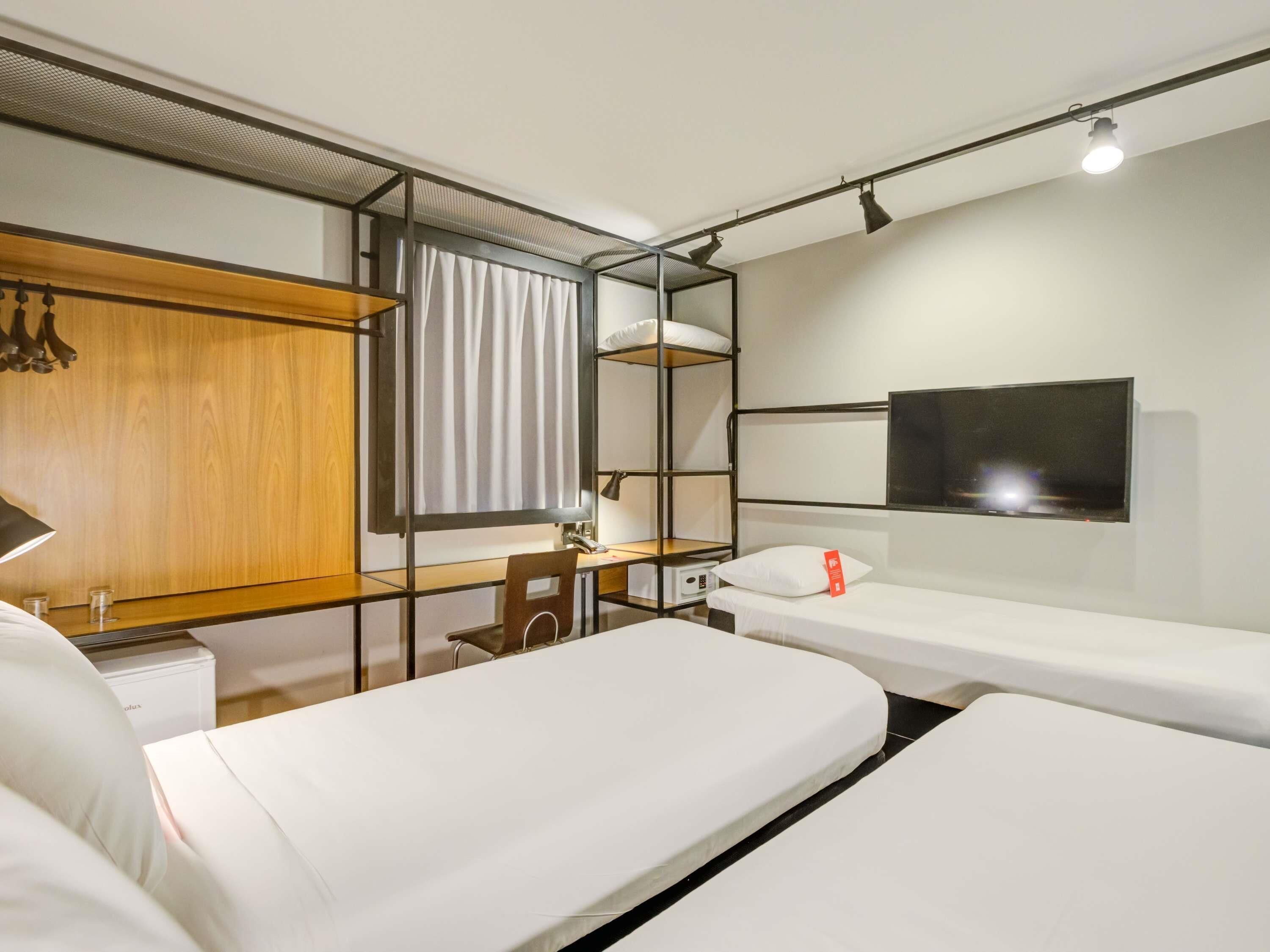 A hotel room with a bed, a desk, a chair, a TV, and a wardrobe.