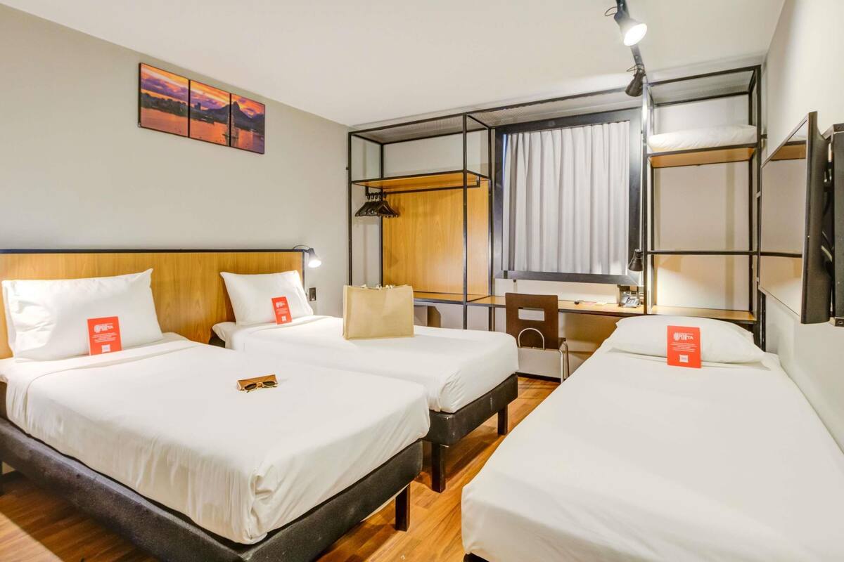 Ein Hotelzimmer mit zwei Betten, einem Schreibtisch, einem Stuhl, einem Spiegel und einem Bild an der Wand.
