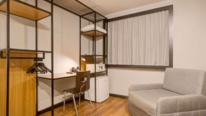 Une pièce de taille modeste, comprenant un bureau en bois, une chaise, un lit et une fenêtre avec des rideaux.