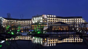 A modern hotel with multiple buildings, a reflective pond, and illuminated trees.