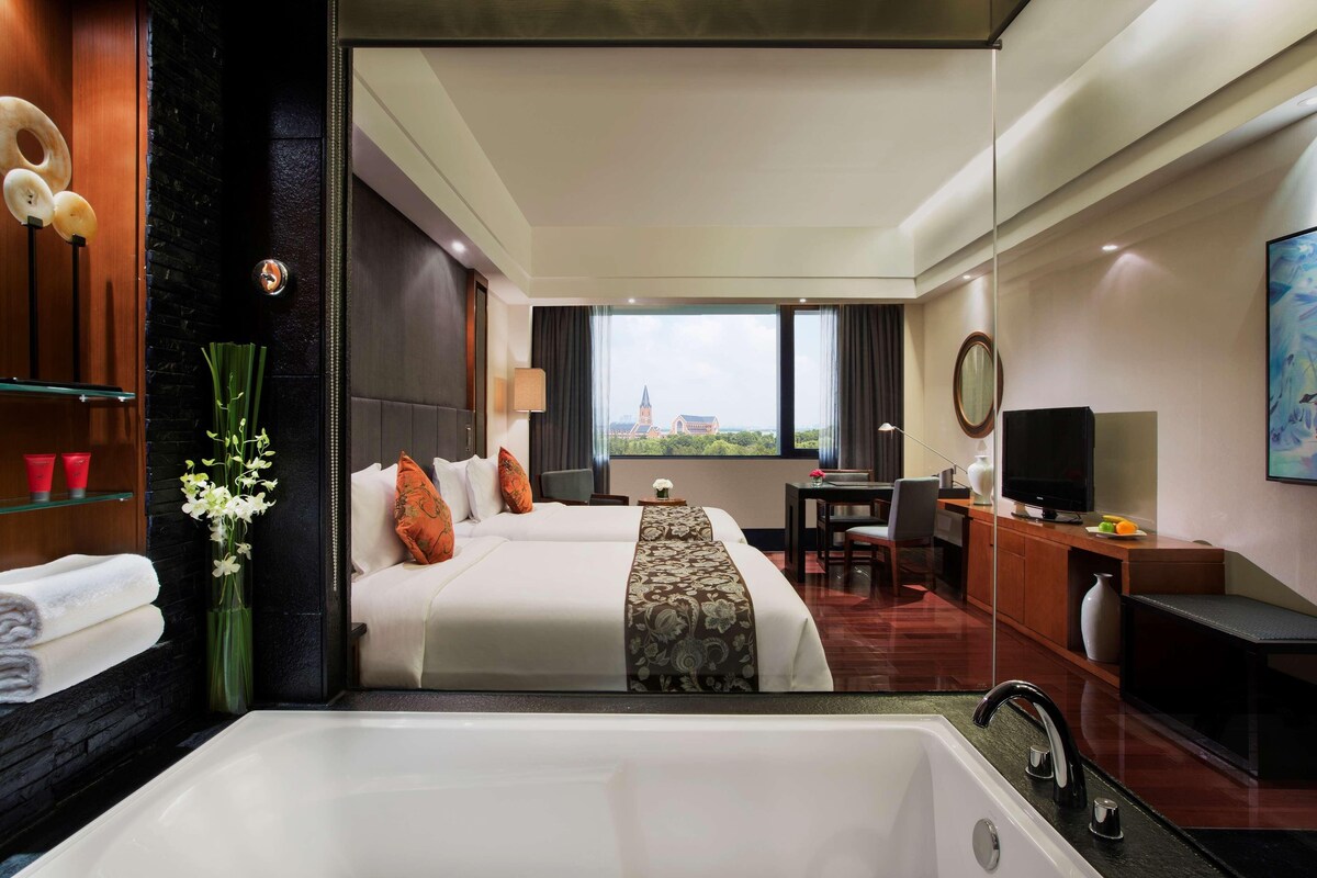 Une chambre d’hôtel avec un grand lit, un bureau, une télévision et une vue sur un immeuble par la fenêtre.