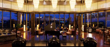 A spacious lobby with a grand piano, large vases, and modern chandeliers.