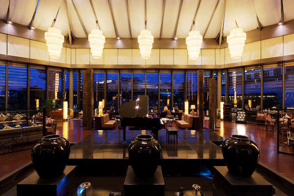 A spacious lobby with a grand piano, large vases, and modern chandeliers.