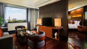 Una habitación de hotel moderna con un ventanal grande, un televisor de pantalla plana, un sofá, una mesa de comedor y una cama con una mesita de noche.