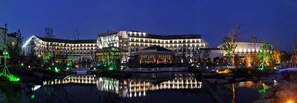 A multi-story hotel with a reflective pool in front, surrounded by trees and illuminated by ambient lighting. - Worldhotel Grand Dushulake Suzhou (Suzhou)