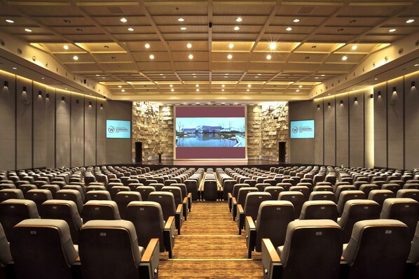 A conference room with rows of chairs, a large screen at the front, and a stone wall backdrop. - Worldhotel Grand Dushulake Suzhou (Suzhou)