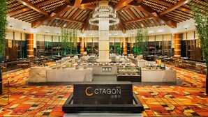 A spacious hotel lobby with a central column, multiple dining areas, and a patterned floor.