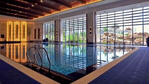 An indoor swimming pool with clear glass walls, metal railings, and a blue textured floor.