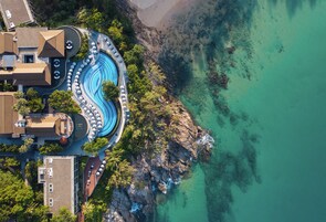 Vista aérea de un complejo turístico con una piscina sinuosa, asientos en la playa y acantilados rocosos.