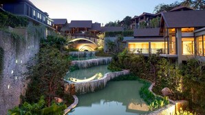 Un resort con varias edificaciones, un puente de piedra y una fuente de agua.