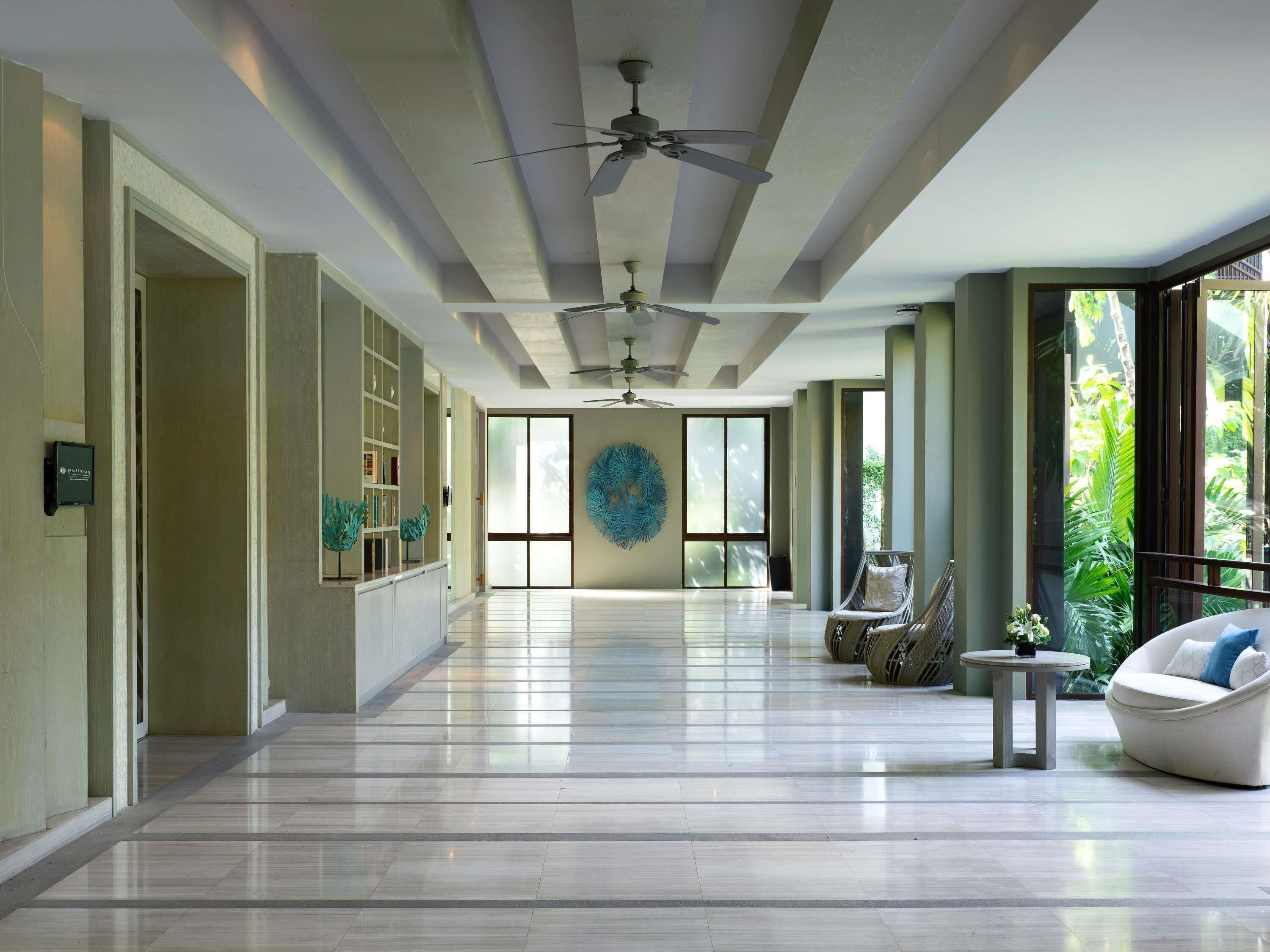A spacious hallway with a ceiling fan, a large window with a view of greenery, and a seating area with a round table and chairs.