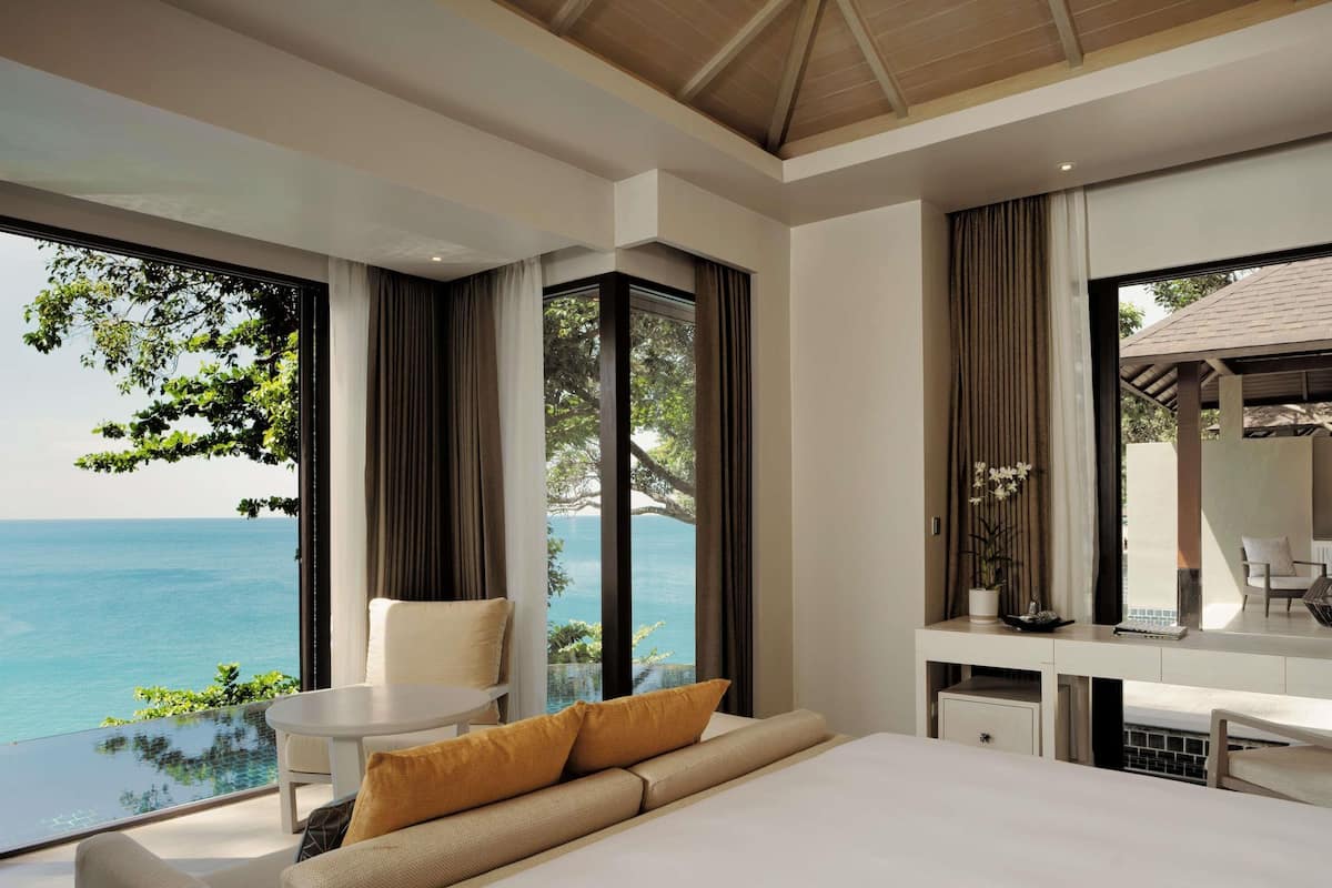 Quarto de hotel moderno com uma cama grande, uma mesinha, uma cadeira e vista para o mar.