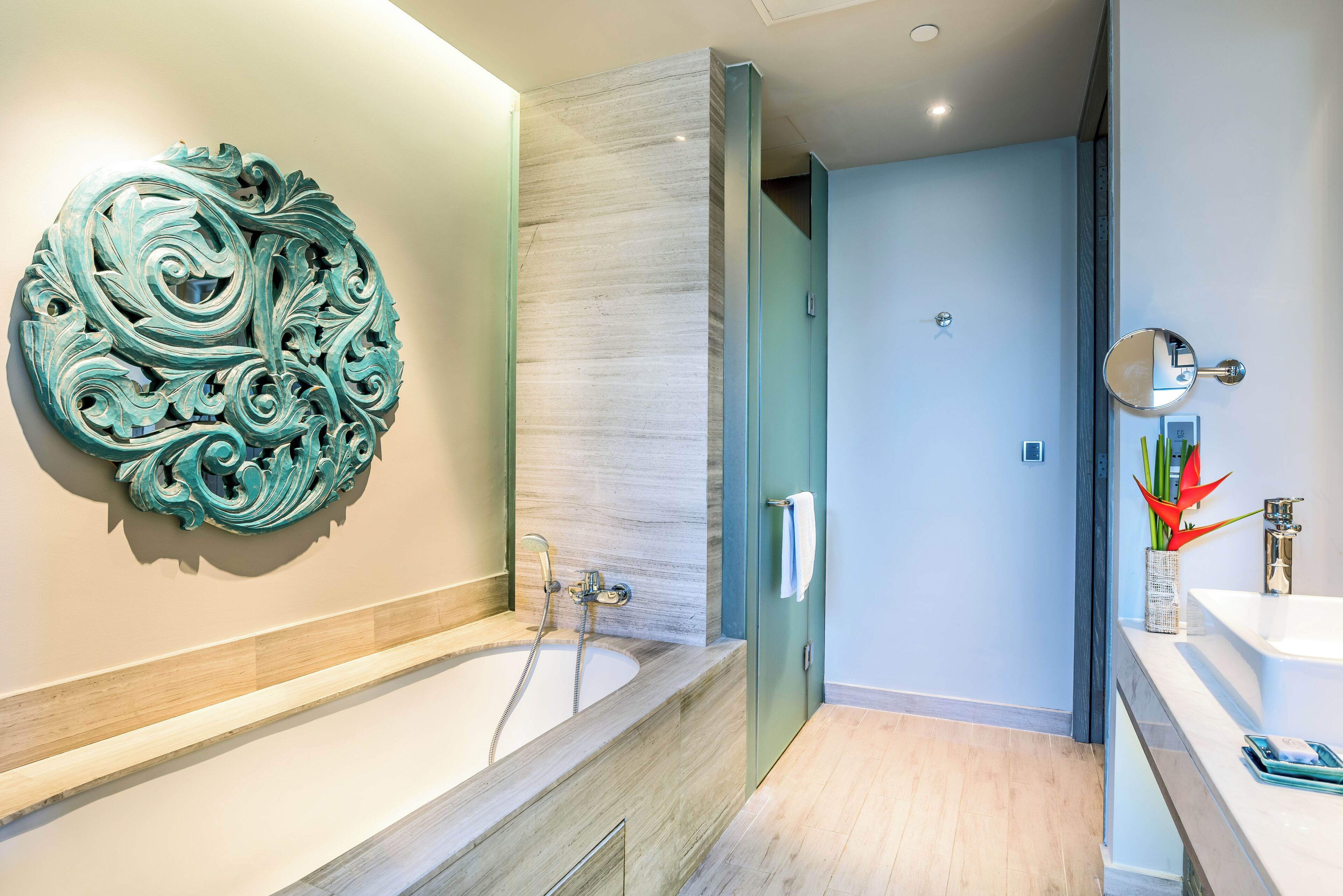 A modern bathroom with a freestanding bathtub, a decorative wall piece, and a mirror with a red flower vase.