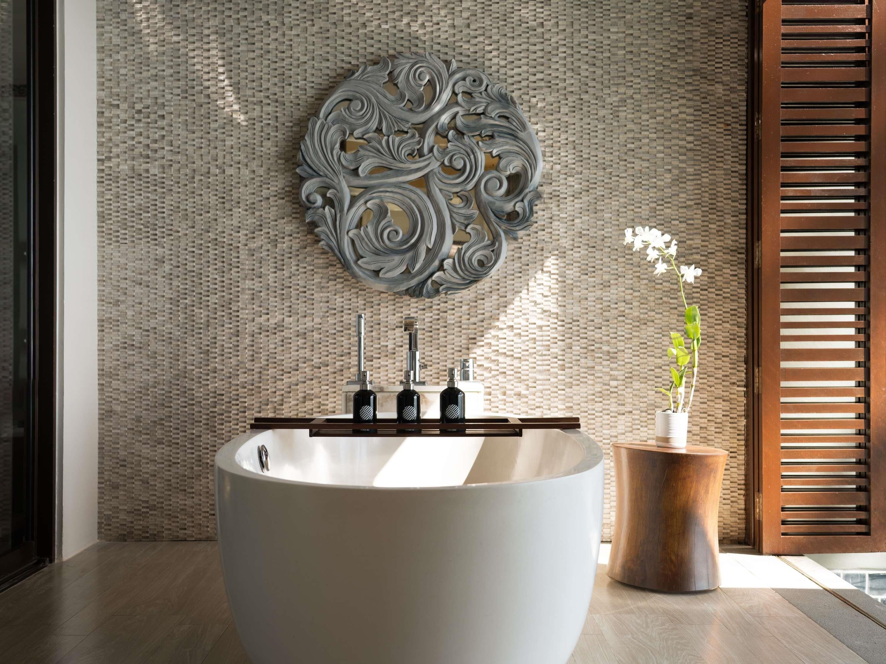 A modern bathroom with a freestanding bathtub, a decorative wall piece, and a potted orchid.