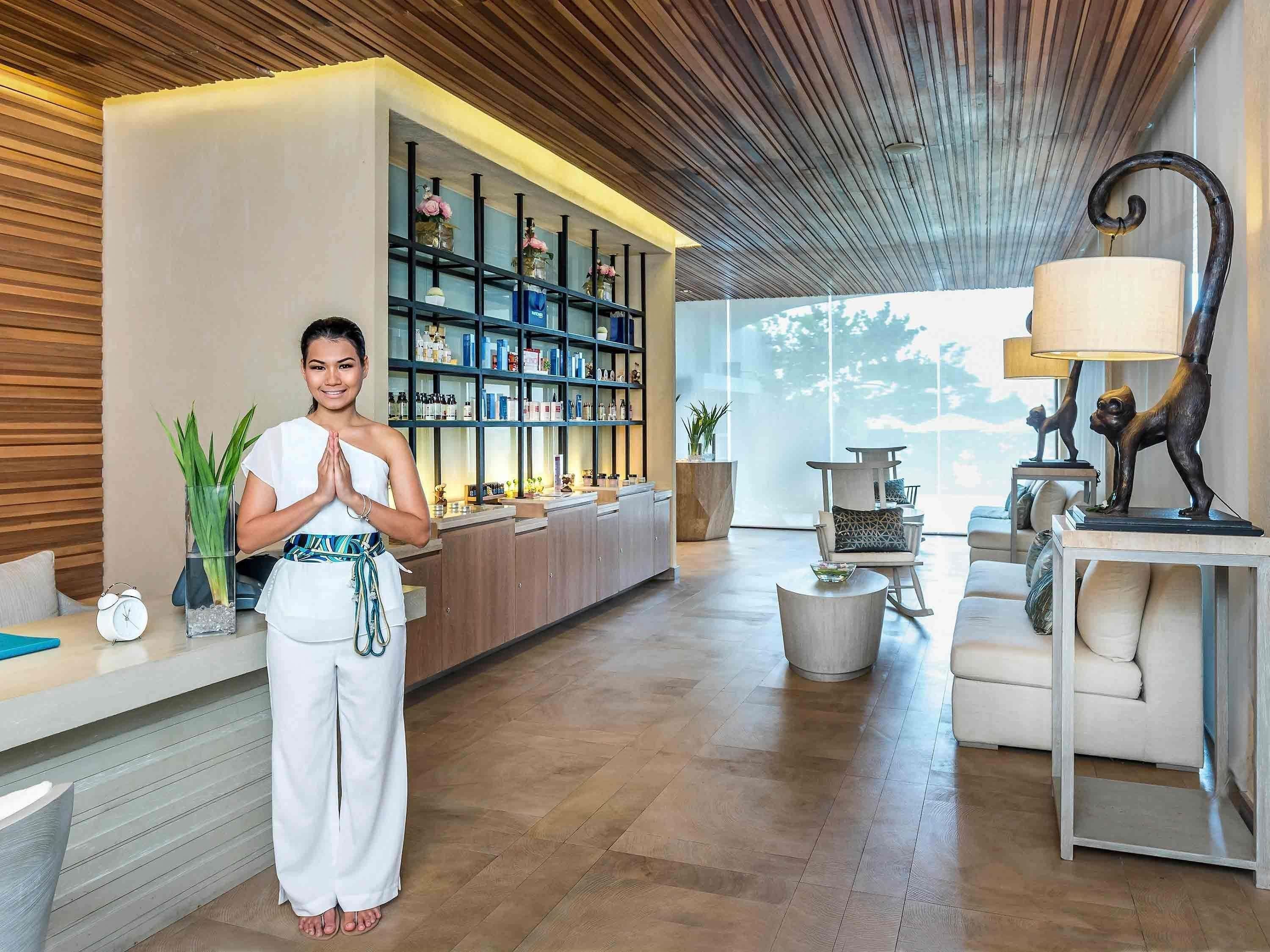 A modern hotel lobby with a reception desk, a large window with a view, and a seating area with a lamp and a statue.