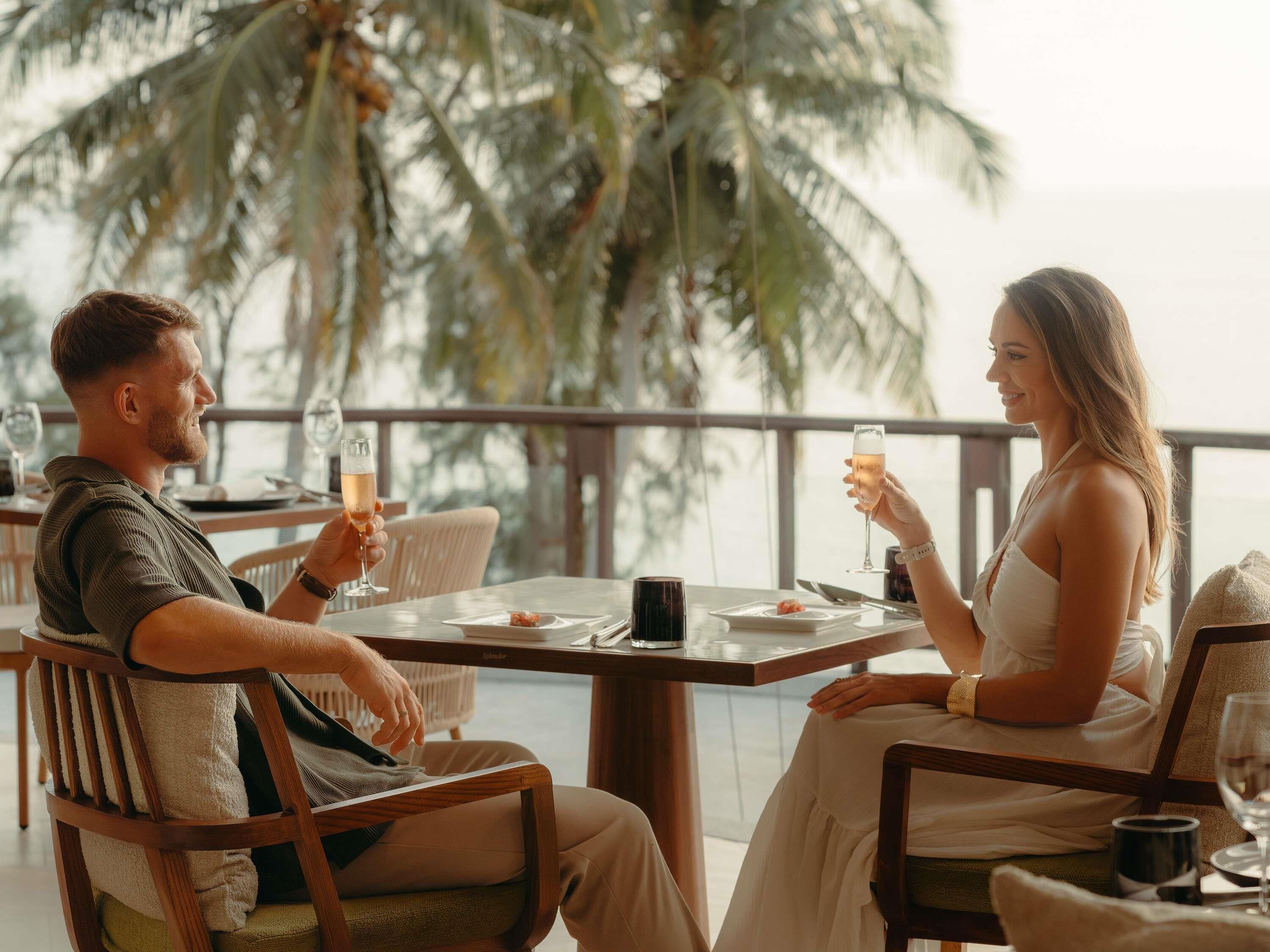 A couple dining at a table with a view of palm trees and the sea.