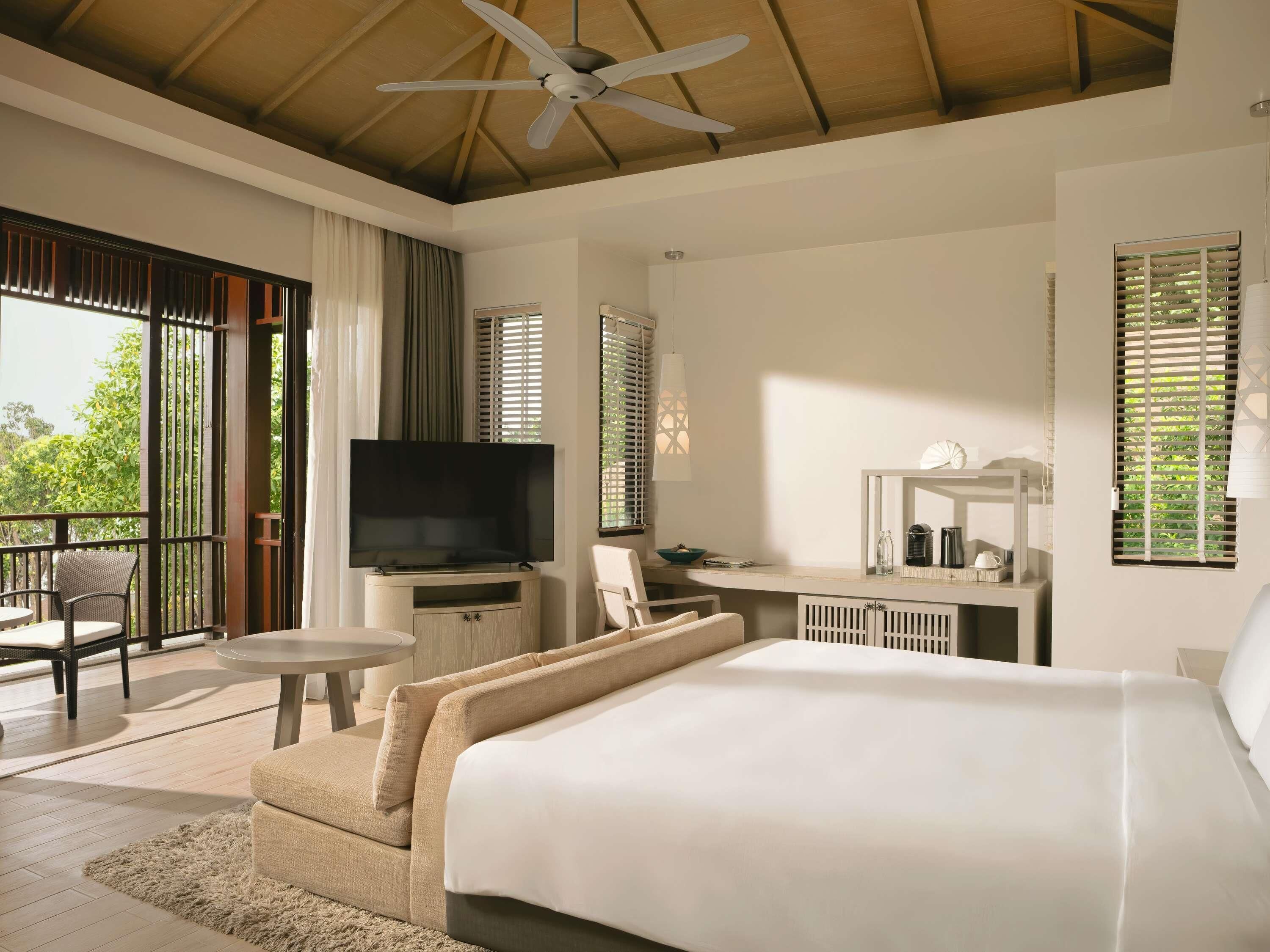 A hotel room with a bed, a TV, a desk, a chair, and a balcony with a view.