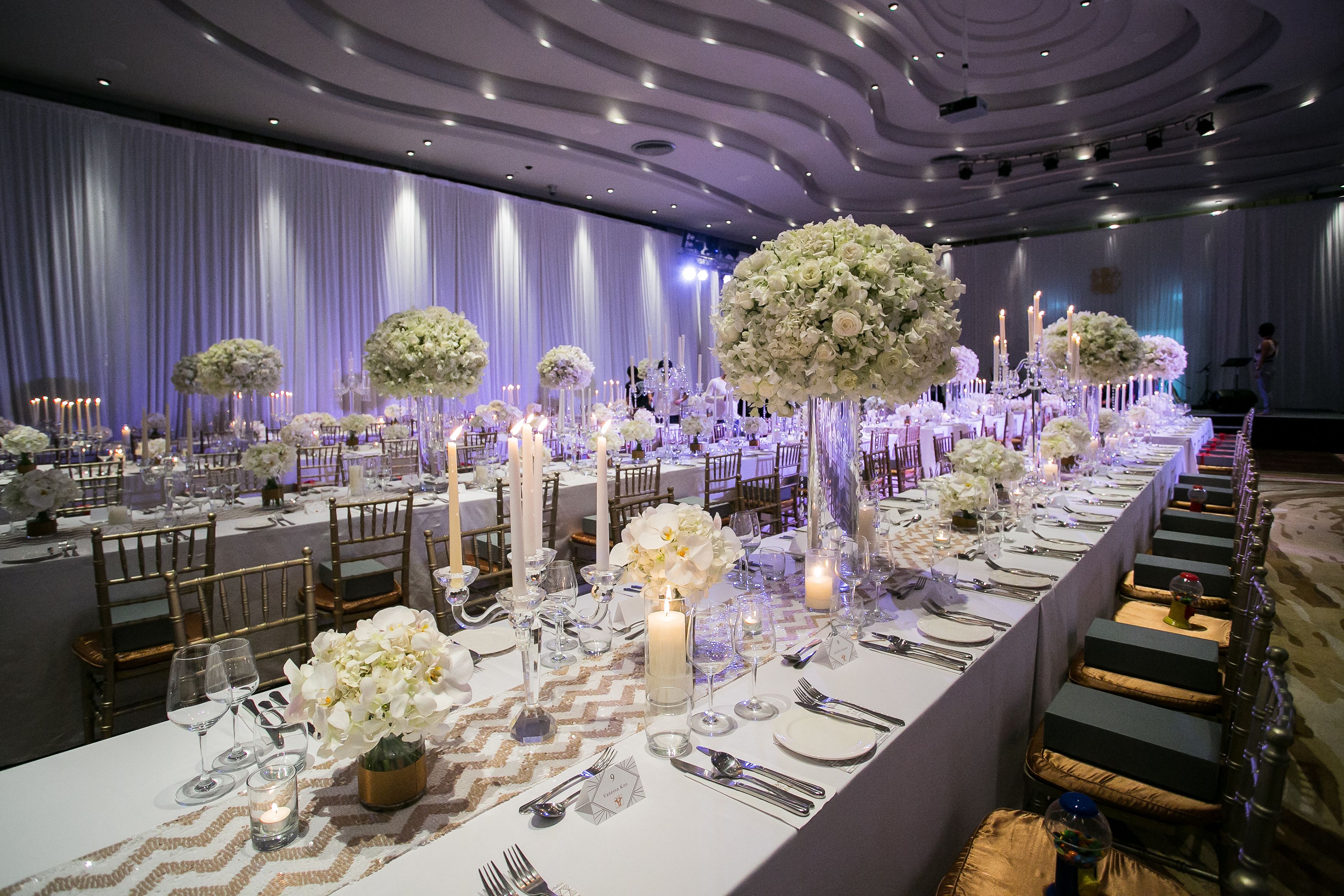 A banquet hall with long tables set for a formal event, featuring floral centerpieces and candles.
