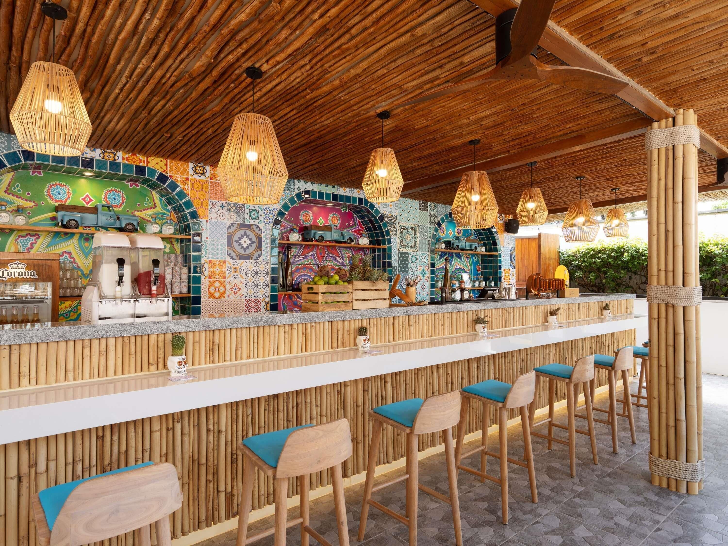A bar area with a wooden ceiling, colorful mosaic wall, and bamboo decor.