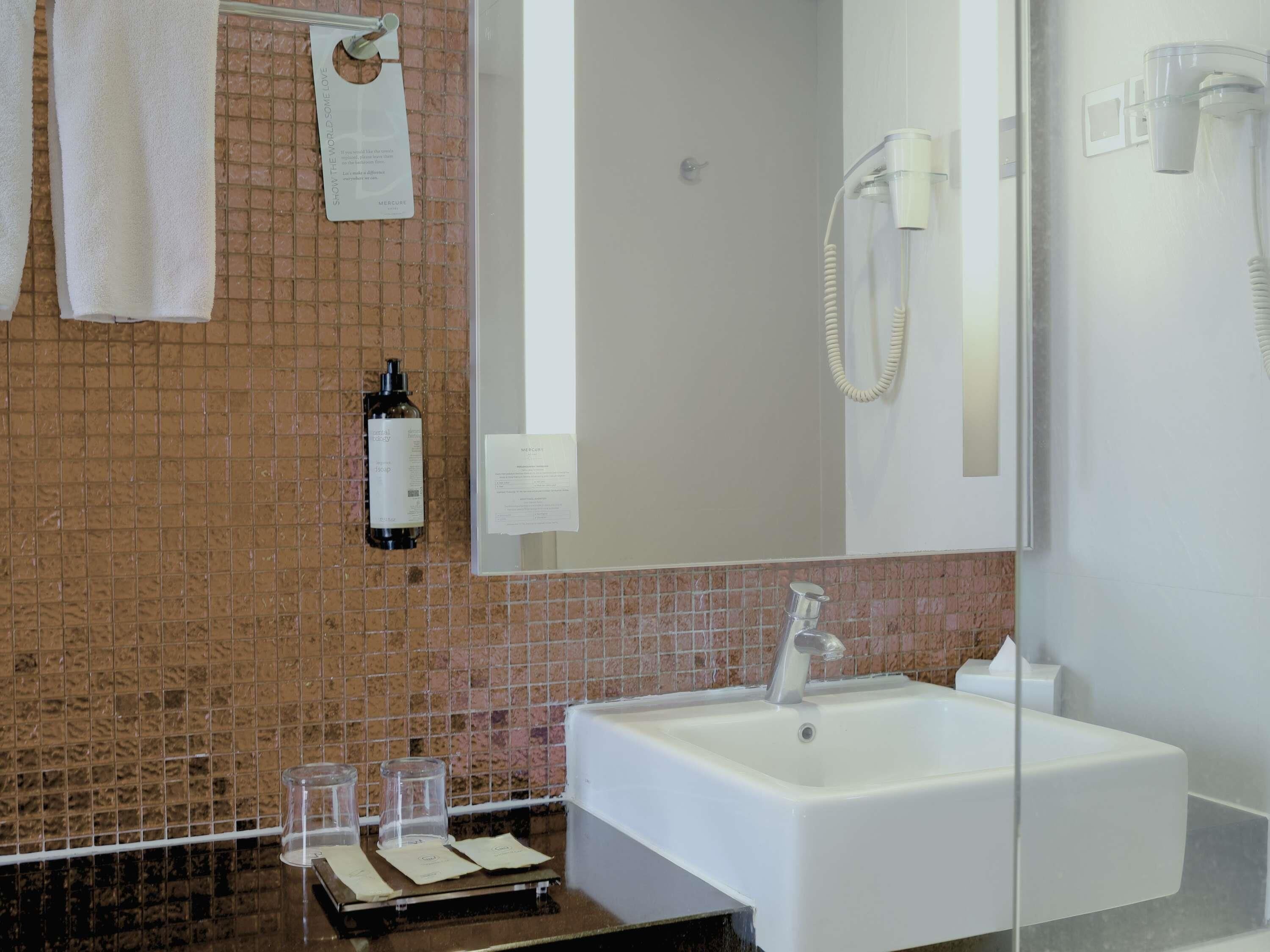 A bathroom with a white sink, a mirror, a towel rack, a bottle of shampoo, and a hairdryer.