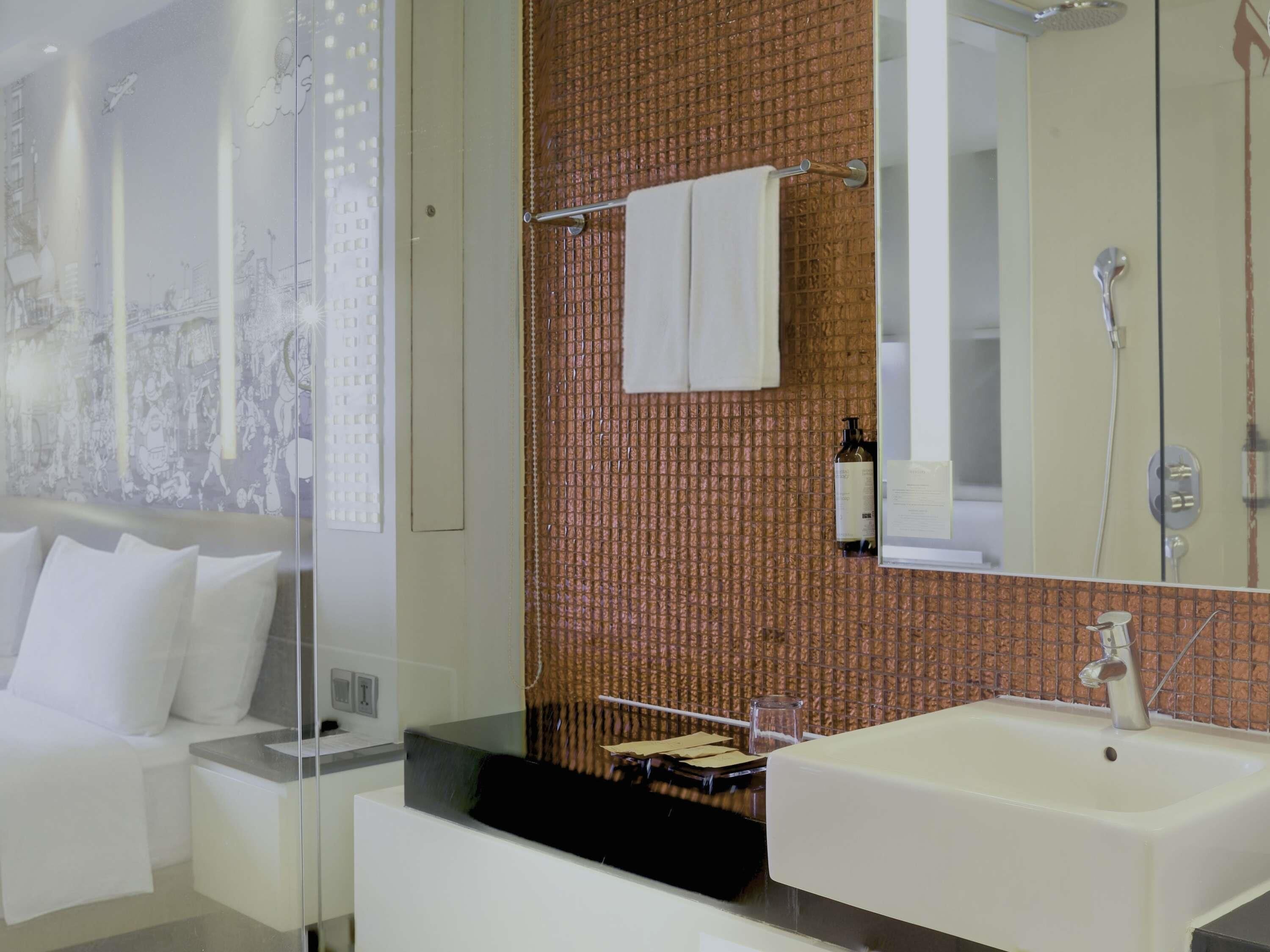 A modern bathroom with a large mirror, a white sink, and a shower.