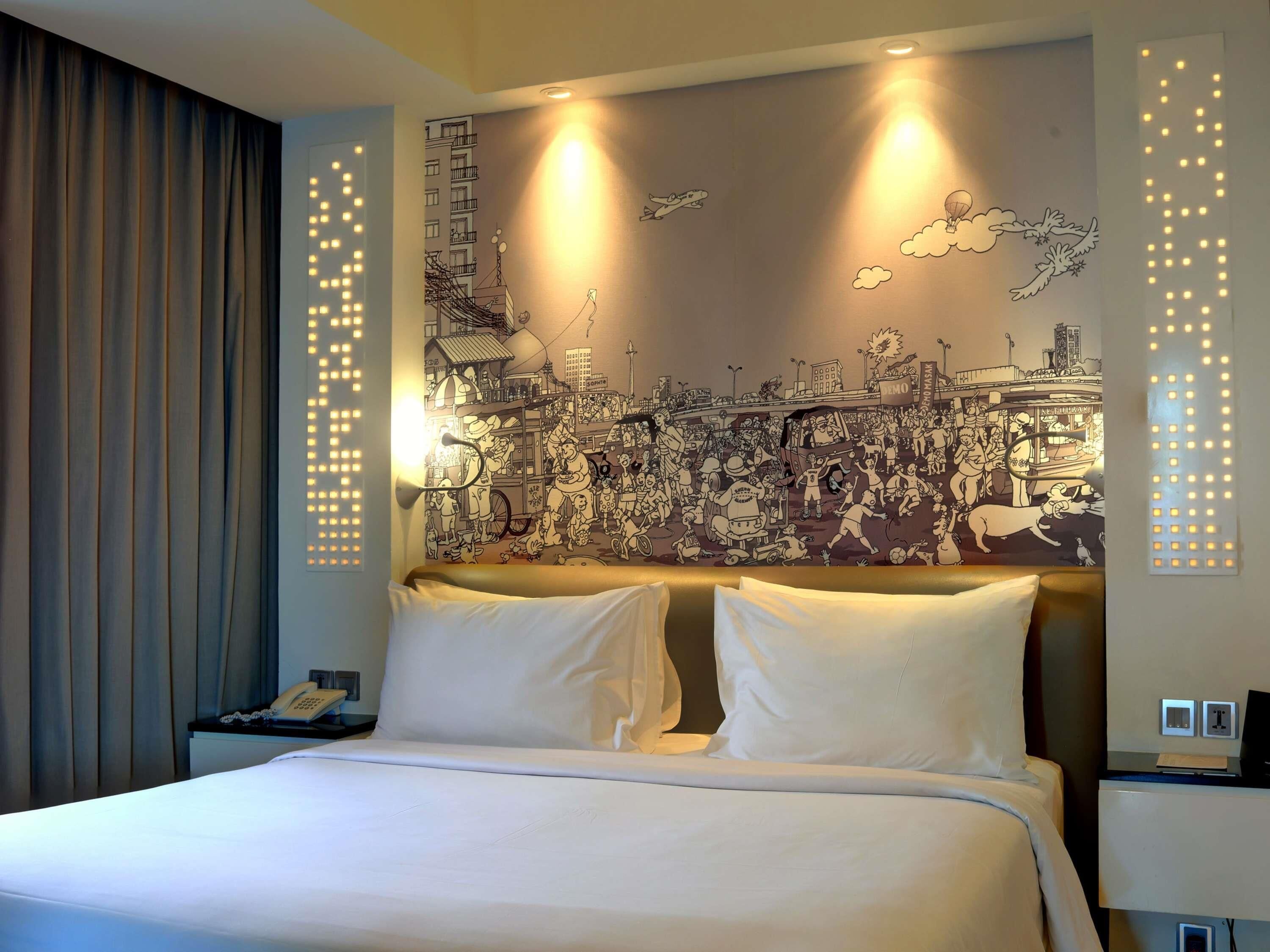 A hotel room with a large bed, a headboard with a cityscape mural, bedside lamps, and a telephone on the nightstand.