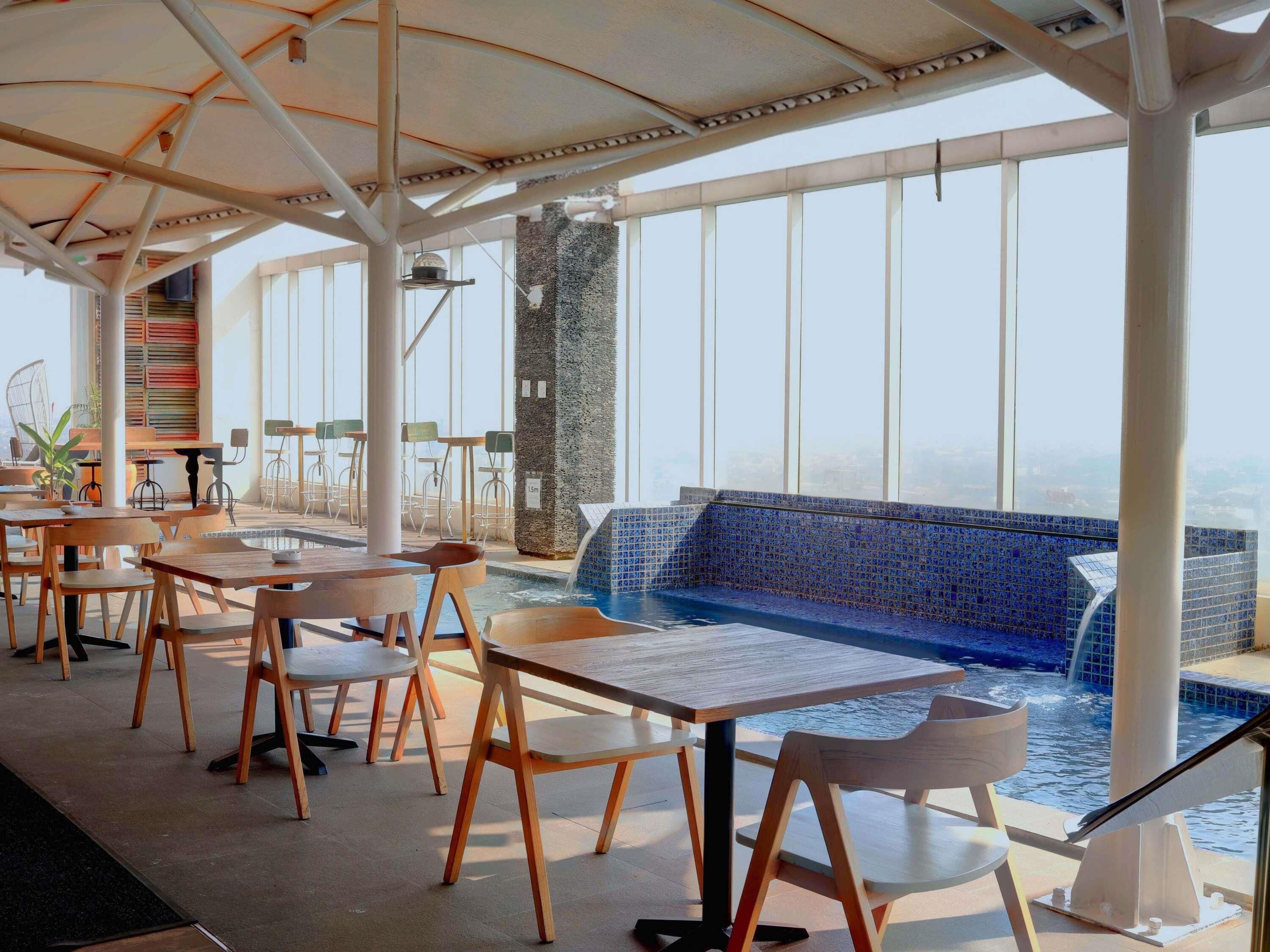 A rooftop bar with tables and chairs, a pool with blue mosaic tiles, and a city view.