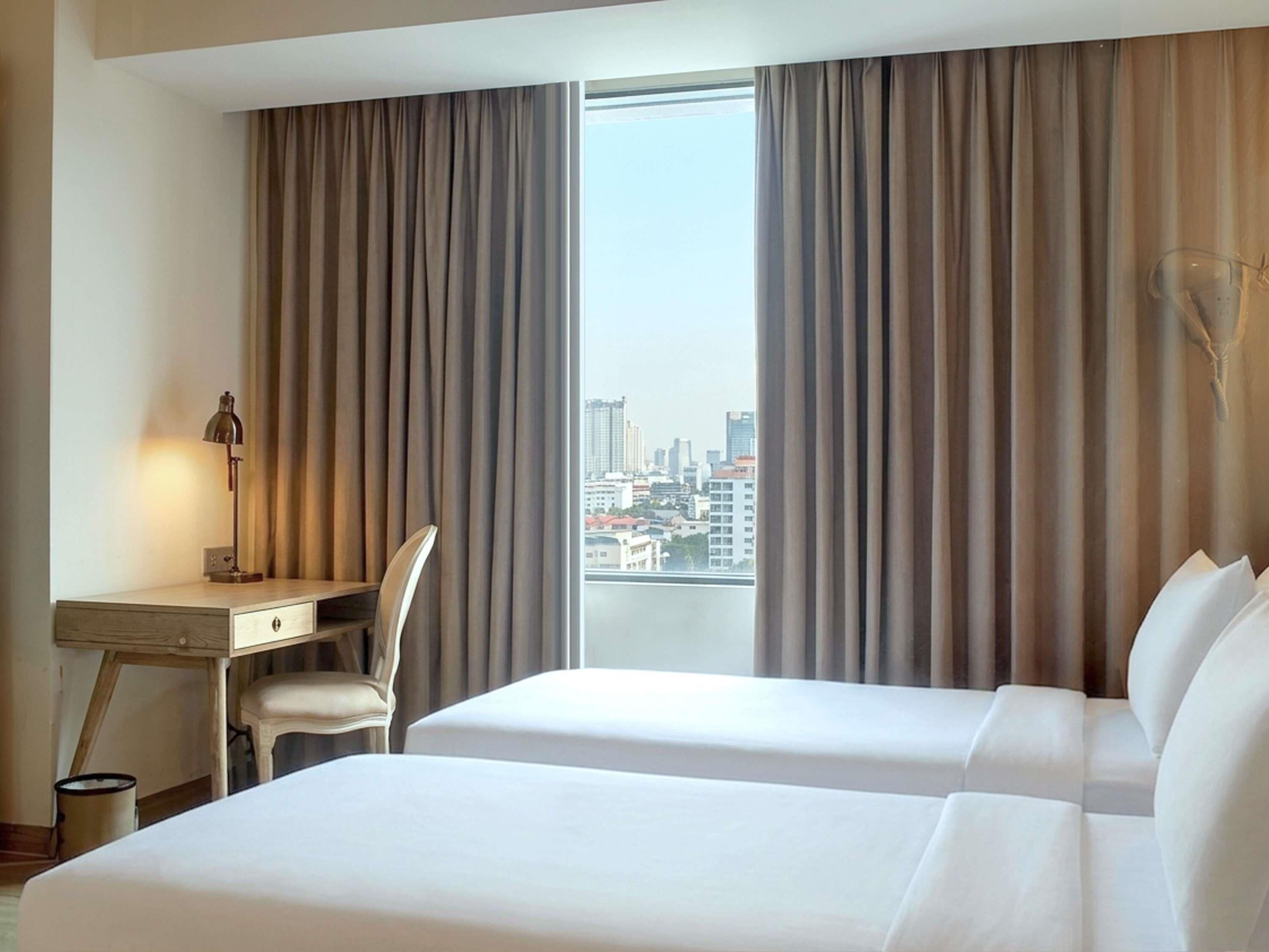 Een hotelkamer met twee bedden, een bureau, een stoel en uitzicht op een stadsgezicht.