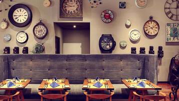 A dining area with multiple tables and chairs, a variety of wall clocks, and a neutral-toned sofa.