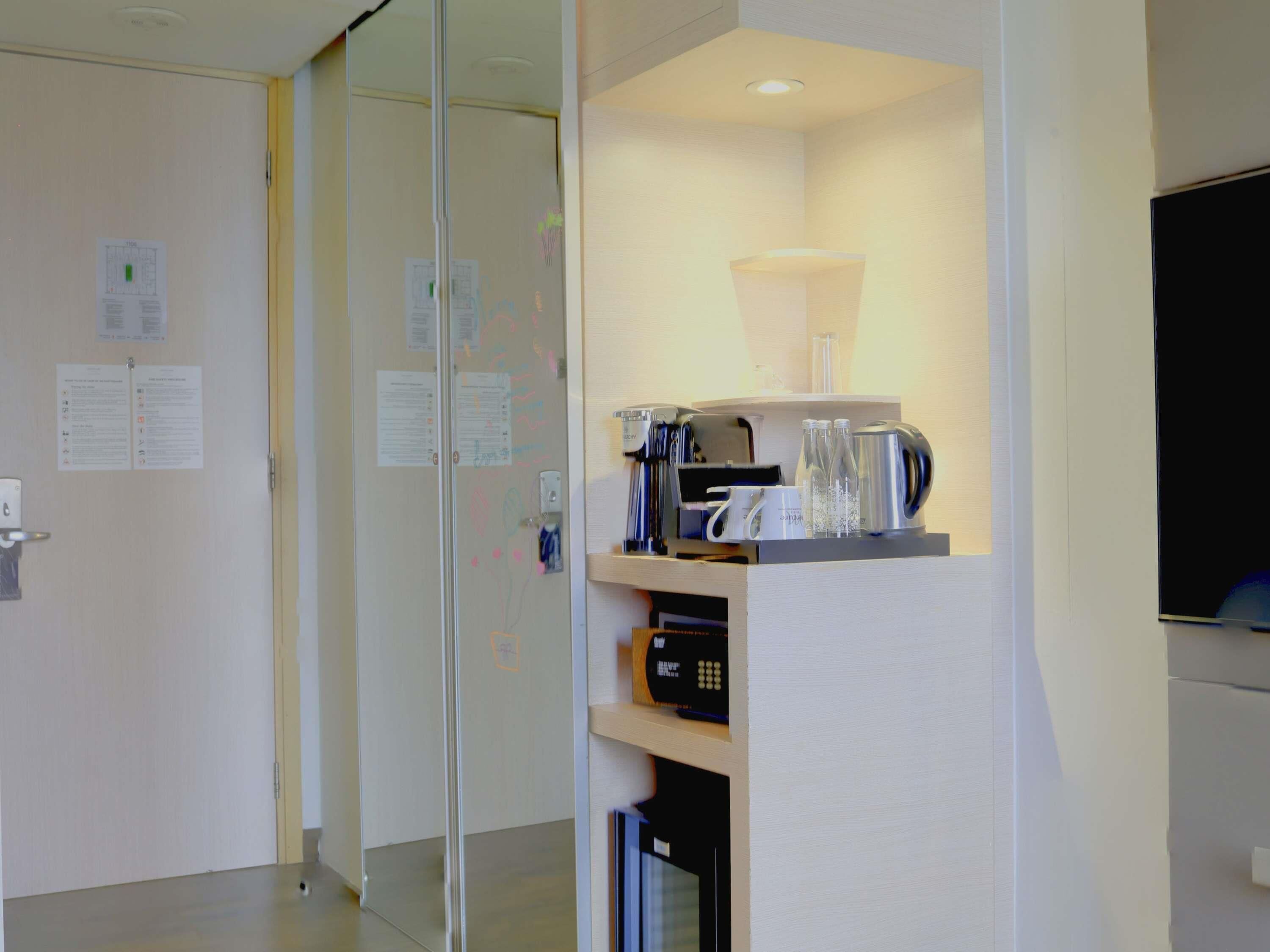 A modern hotel room with a glass partition, a coffee station, and a flat-screen TV.